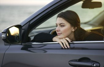 Pensive Caucasian woman leaning in car window