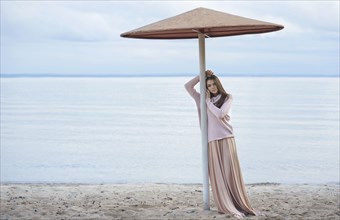 Pensive Caucasian woman leaning on beach umbrella