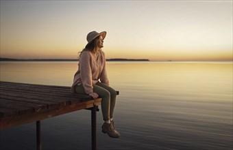 Caucasian woman sitting on dock of lake admiring sunset