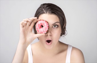 Surprised Caucasian woman holding donut over eye