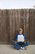 Mixed race boy typing on laptop outdoors
