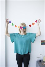 Caucasian woman covering eyes with string of paper hearts