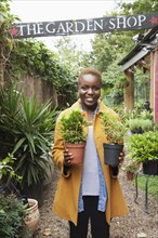 Portrait of smiling Black woman holding potted plants