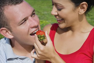 Hispanic woman feeding strawberry to boyfriend