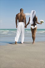 African bride and groom holding hands at beach