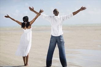 Multi-ethnic couple with arms raised at beach