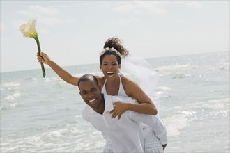 Multi-ethnic bride and groom playing at beach