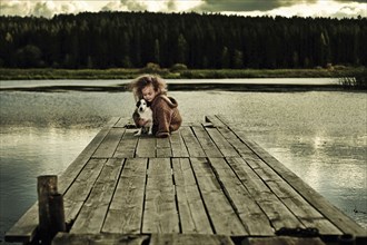 Caucasian girl with dog on wooden deck in still lake