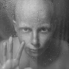 Caucasian woman peering through wet glass