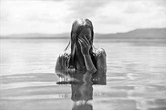 Caucasian teenage girl covering her face in lake
