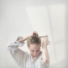 Caucasian teenage girl tying her hair into bun