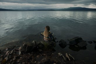 Caucasian girl sitting on rocks at lake
