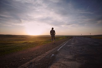 Caucasian man standing near cracked road at sunset
