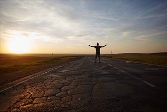 Caucasian man standing in cracked road at sunset with arms outstretched