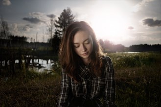 Pensive Caucasian woman in field near lake