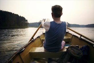Caucasian man paddling in rowboat at sunset