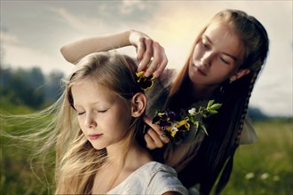 Caucasian girl placing flower in hair of sister