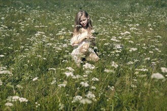 Caucasian girl crouching in field picking wildflowers