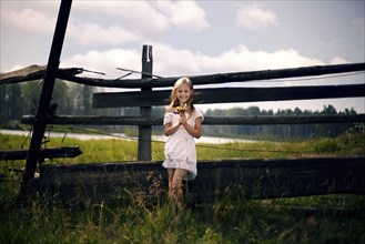 Caucasian girl holding bouquet of wildflowers leaning on wooden fence