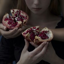 Intertwined Caucasian girls holding sliced pomegranate