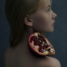 Caucasian girl balancing pomegranate slice on shoulder
