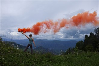 Caucasian girl holding orange smoke flare on mountain range