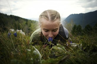 Caucasian girl smelling wildflower laying in grass on hill