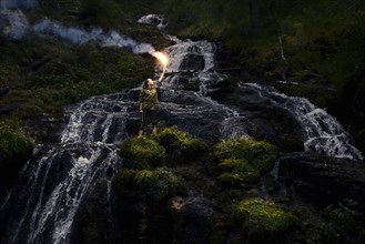 Caucasian girl holding smoke flare near waterfall
