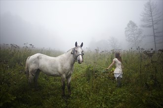 Caucasian girl walking horse in foggy field