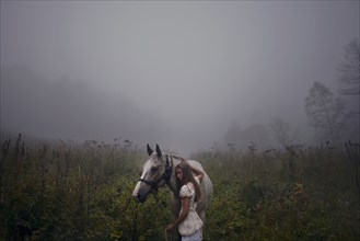 Caucasian girl petting horse in foggy field