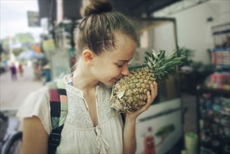 Caucasian woman smelling pineapple at market