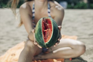 Caucasian woman showing sliced watermelon on beach
