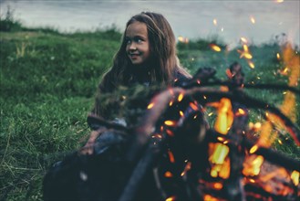 Caucasian girl sitting near campfire