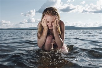 Caucasian teenage girl kneeling in ocean splashing water on face