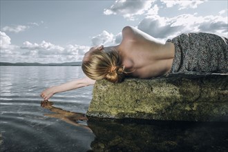 Topless Caucasian teenage girl laying on rock in ocean