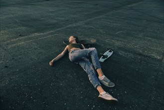 Caucasian teenage girl laying on pavement with head on skateboard