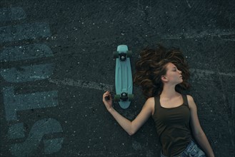 Caucasian teenage girl laying on pavement with skateboard