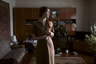Pensive Caucasian woman standing in livingroom