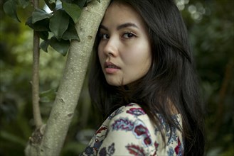 Portrait of Asian woman leaning forehead on tree branch