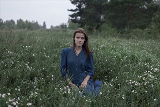 Serious Caucasian teenage girl sitting in field of wildflowers