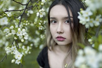 Asian teenage girl standing in branches with flowers