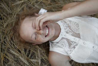 Smiling Caucasian girl with freckles laying in wheat