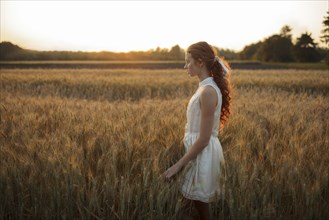Pensive Caucasian girl standing in field of wheat