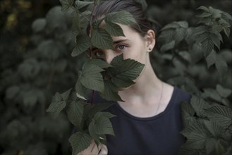 Face of Caucasian teenage girl behind leaves