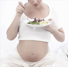Pregnant Caucasian woman eating salad