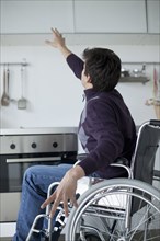 Caucasian man in wheelchair reaching for kitchen cabinet