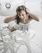 Hispanic woman ignoring alarm clock in bed
