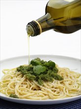 Bottle of olive oil pouring over plate of pesto pasta