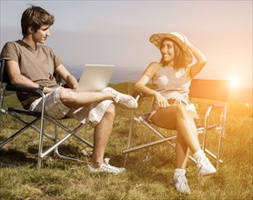 Couple using laptop in field on folding chairs