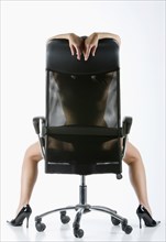 Naked Caucasian woman wearing high heels in office chair